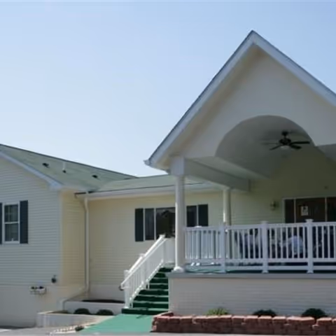 Senior living facility entrance with covered front porch, stairs, and white railing.