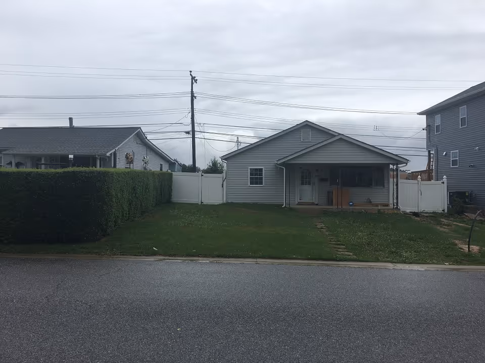 Residential single-story building with front porch, manicured lawn, and white fencing along the street.