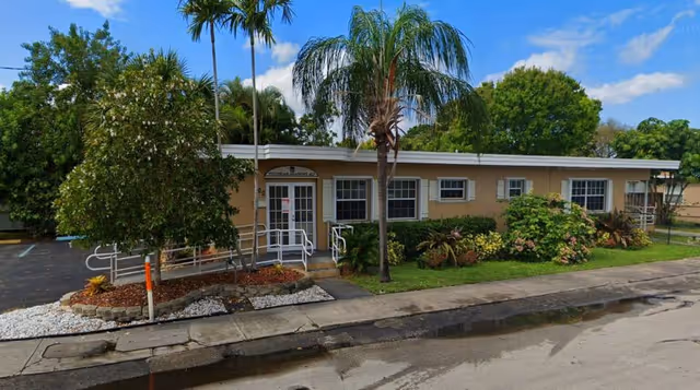 Front view of Victorian Meadows Residence, a single-story beige senior living facility with palm trees.