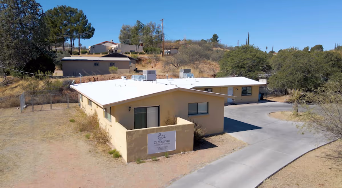 Single-story beige assisted-living building with Cimarron sign, driveway, and desert landscaping.