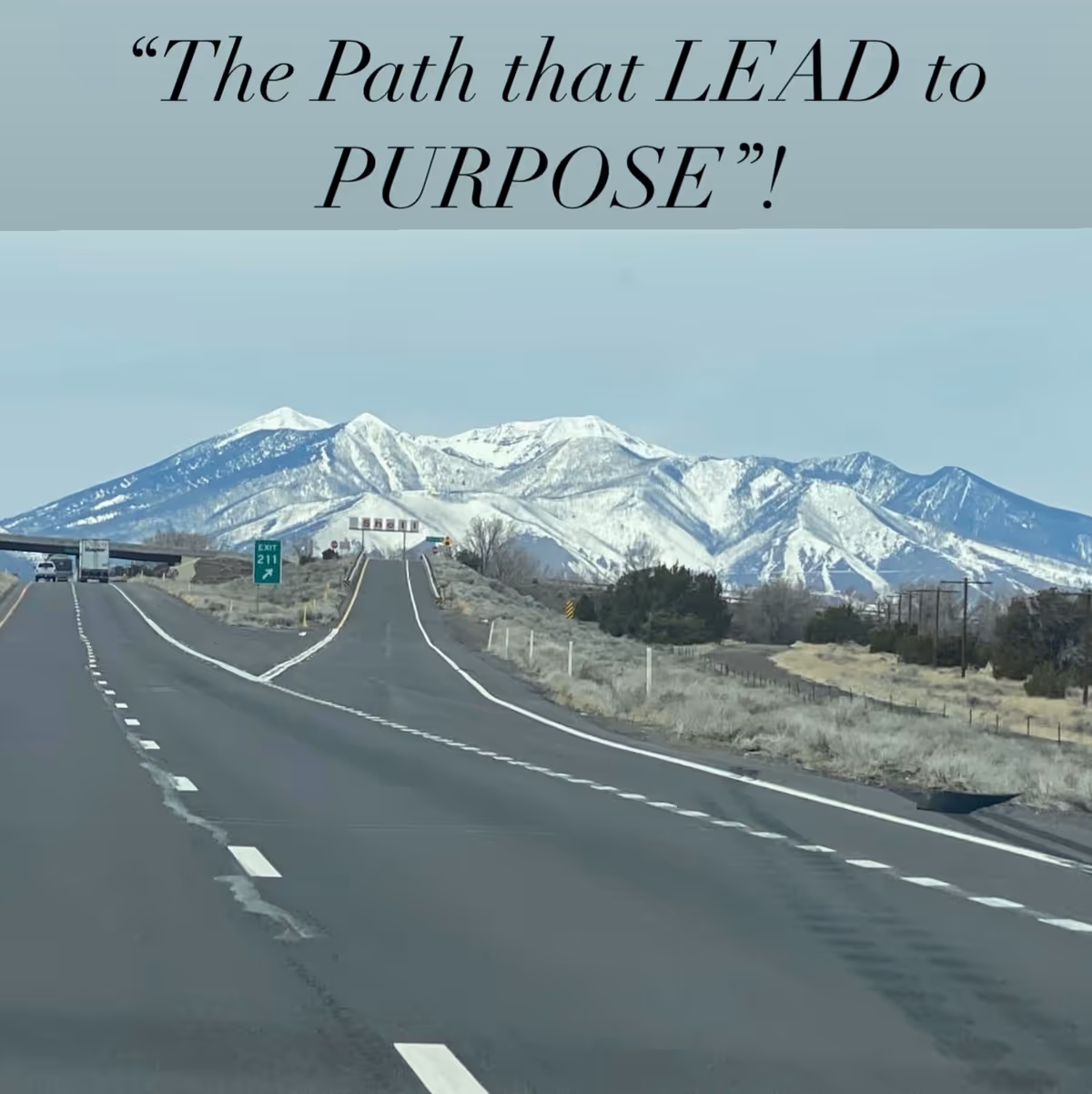 Long road toward snow-capped mountains with a blue banner overhead.
