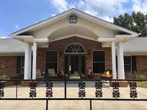 Front entrance of a brick assisted living facility with white columns and decorative railing.