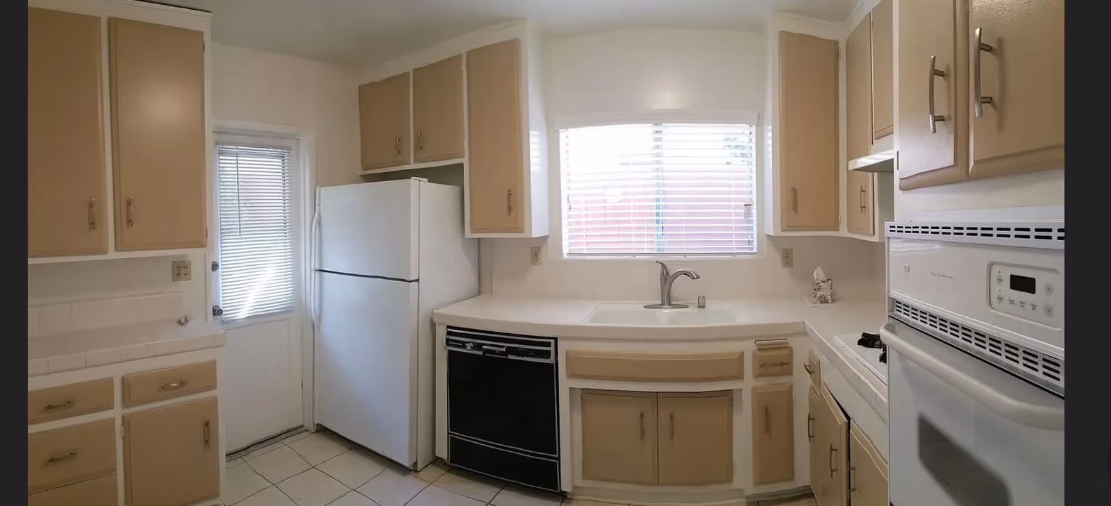 A small, light-toned kitchen with cabinets, white countertops, sink, stove, fridge, and dishwasher.