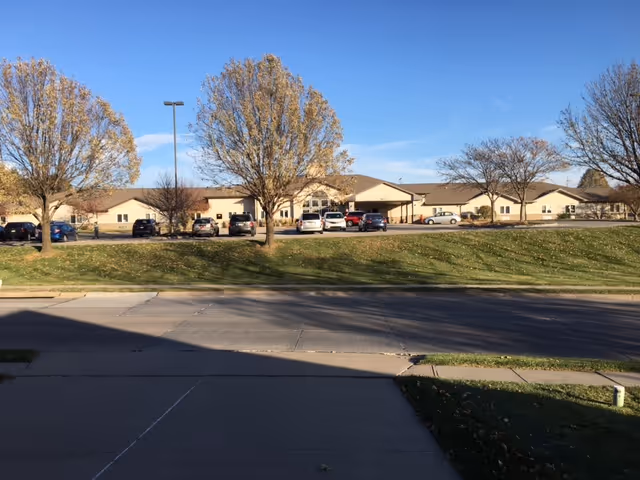 Exterior view of Clement Manor Retirement Community with parking and trees.
