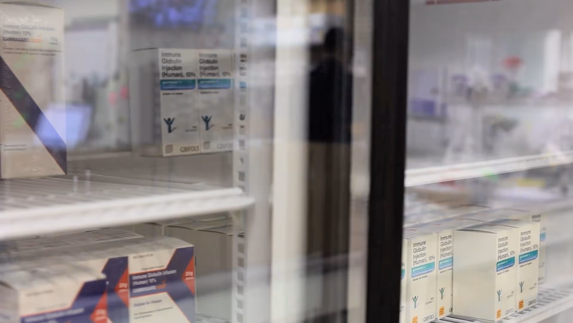 Glass refrigerator doors reveal shelves of boxed vaccines and medical supplies.