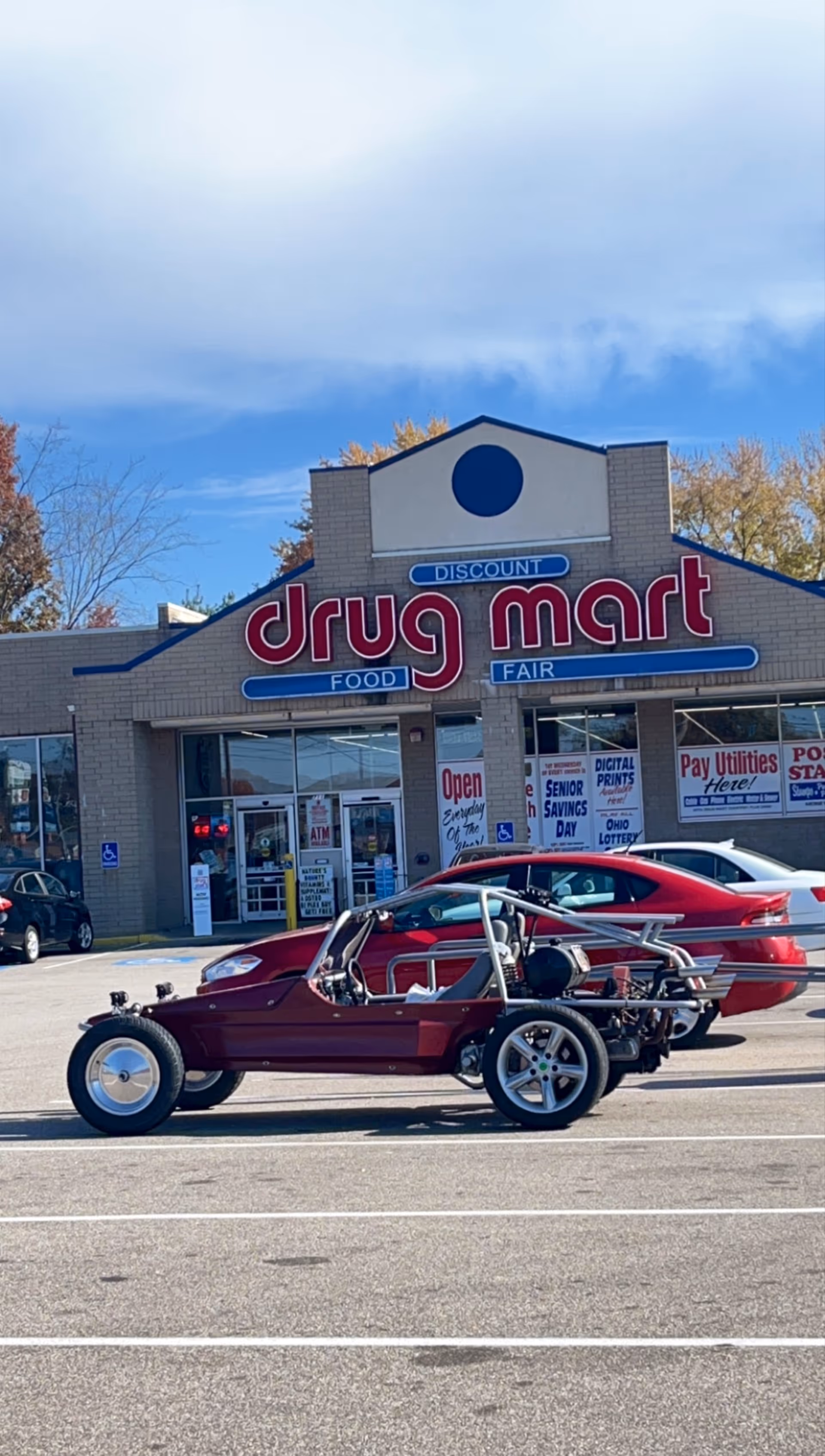Exterior view of Discount Drug Mart storefront with a red custom car parked in front