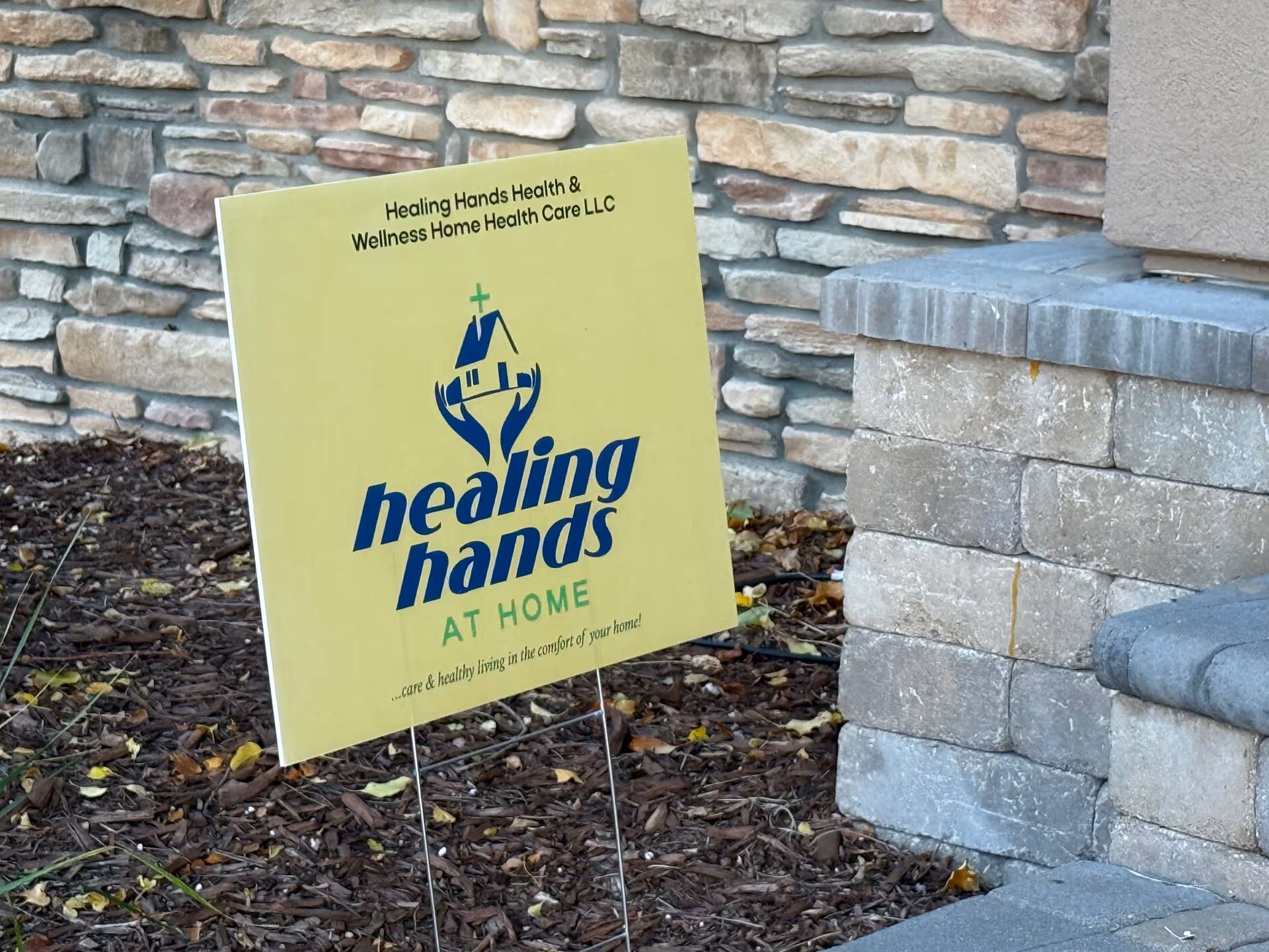 Yellow Healing Hands sign out front against a stone wall and concrete steps.
