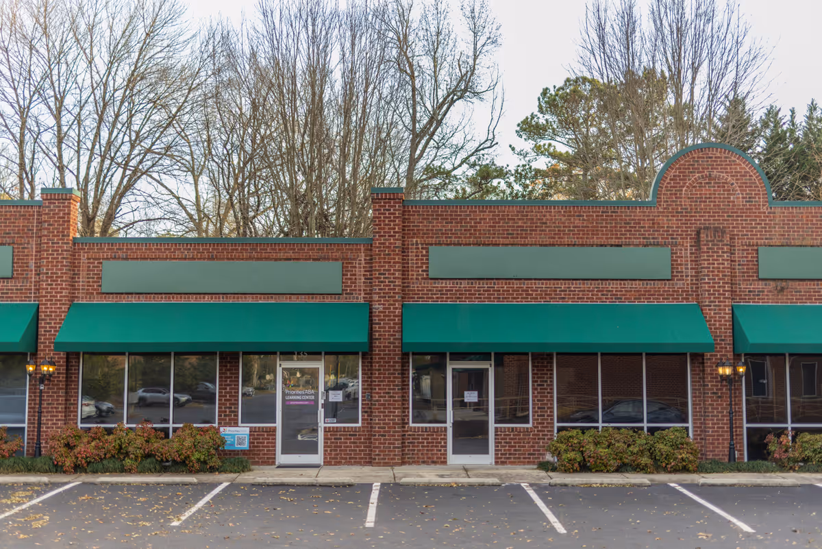 Brick building with green awnings, storefront windows, and a parking lot in front.