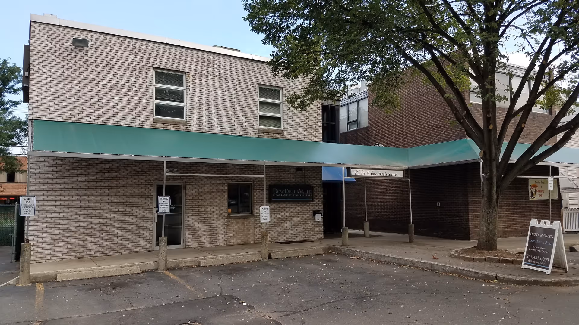 Brick building with green awning, entrance, tree, and adjacent parking area.
