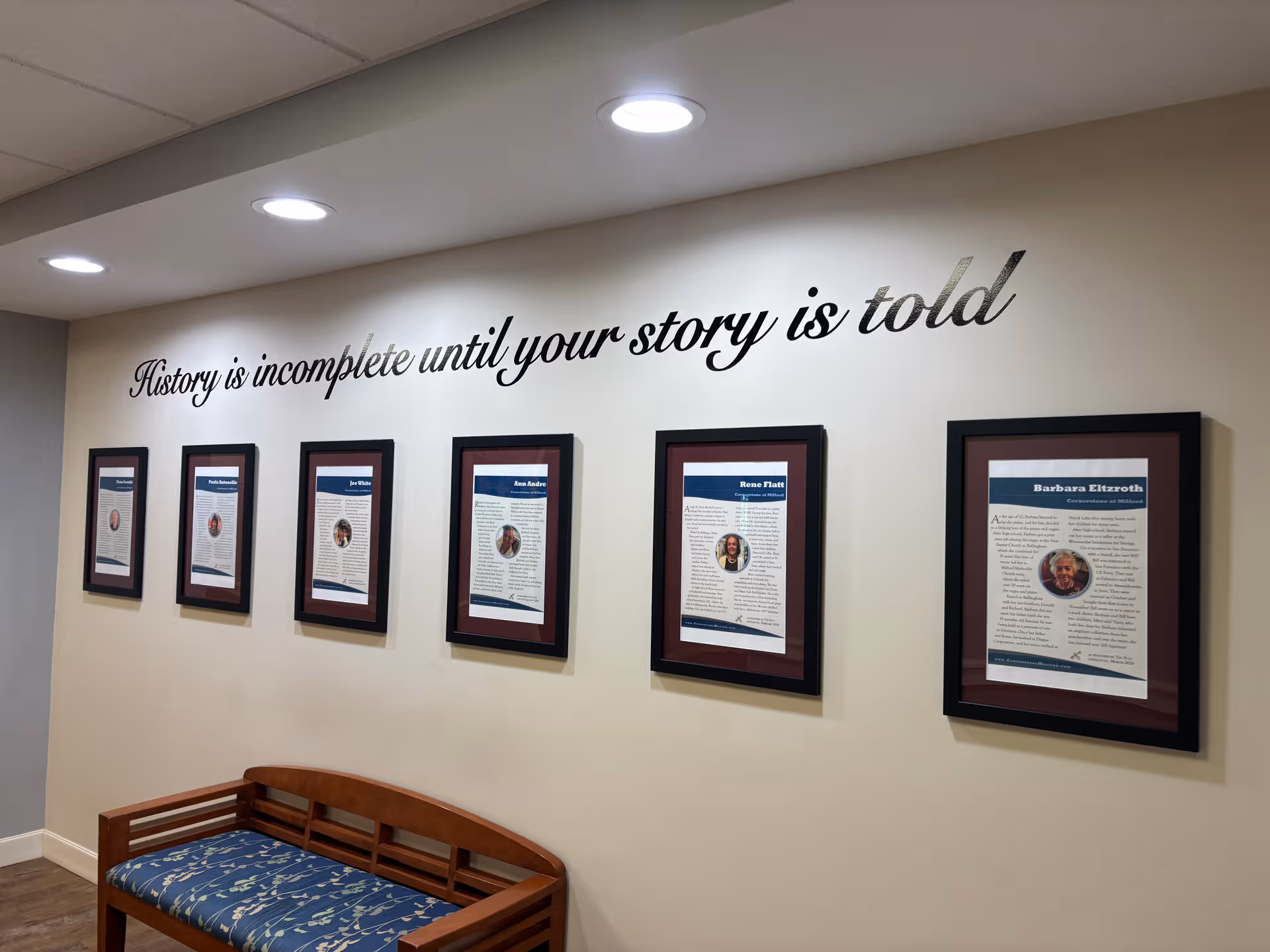 Interior hallway with framed bios on wall and a wooden bench.