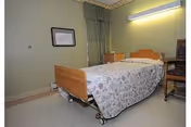 A nursing home patient room with a wheeled bed, curtains, and bedside furniture.