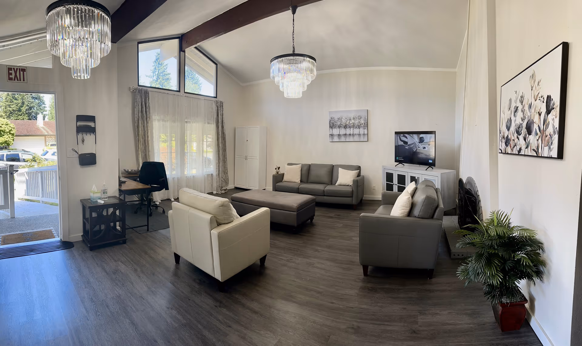 Spacious lounge area with gray sofas, coffee table, chandelier, TV, art, and large windows.