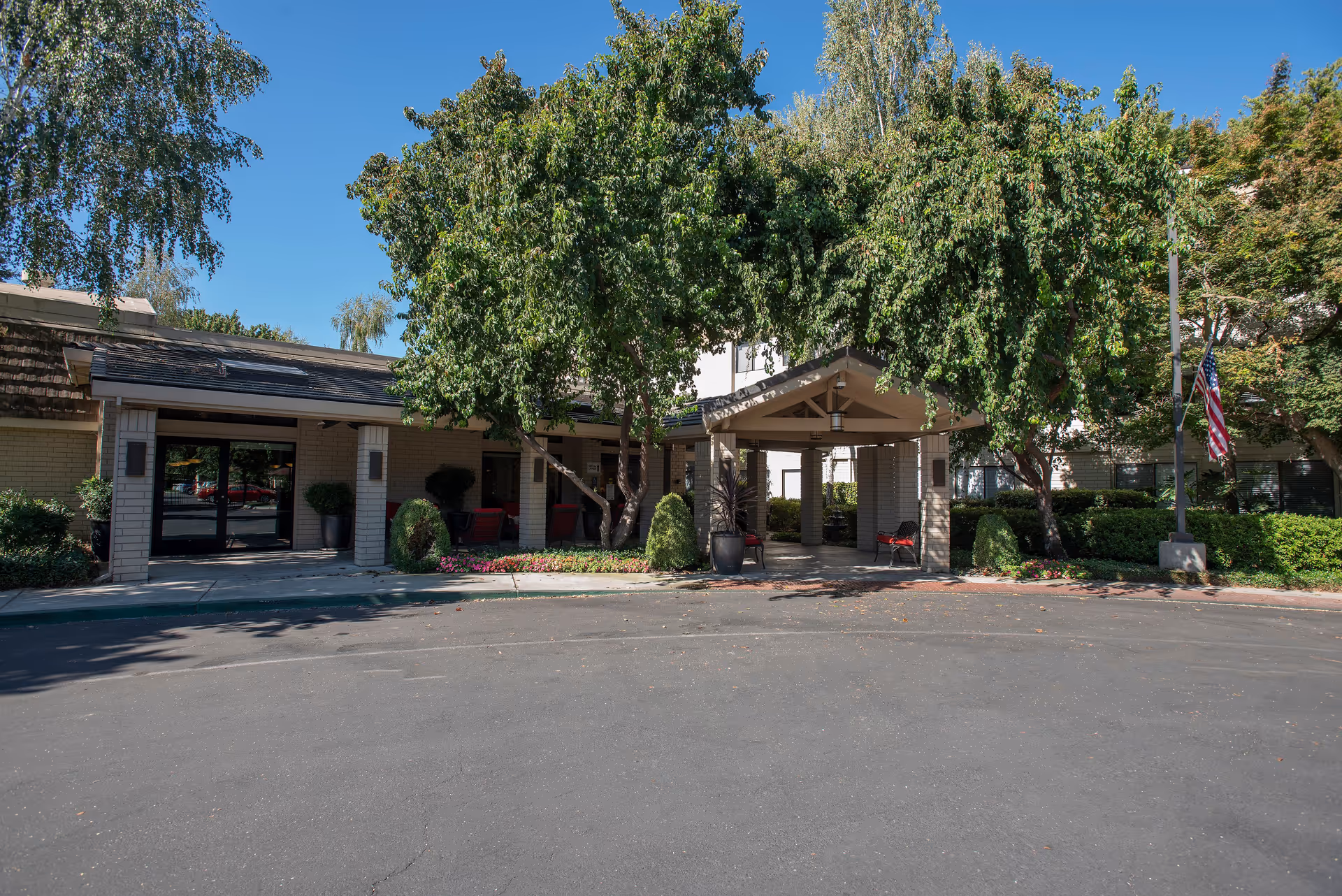 Senior living facility exterior with entrance canopy, trees, and an American flag.