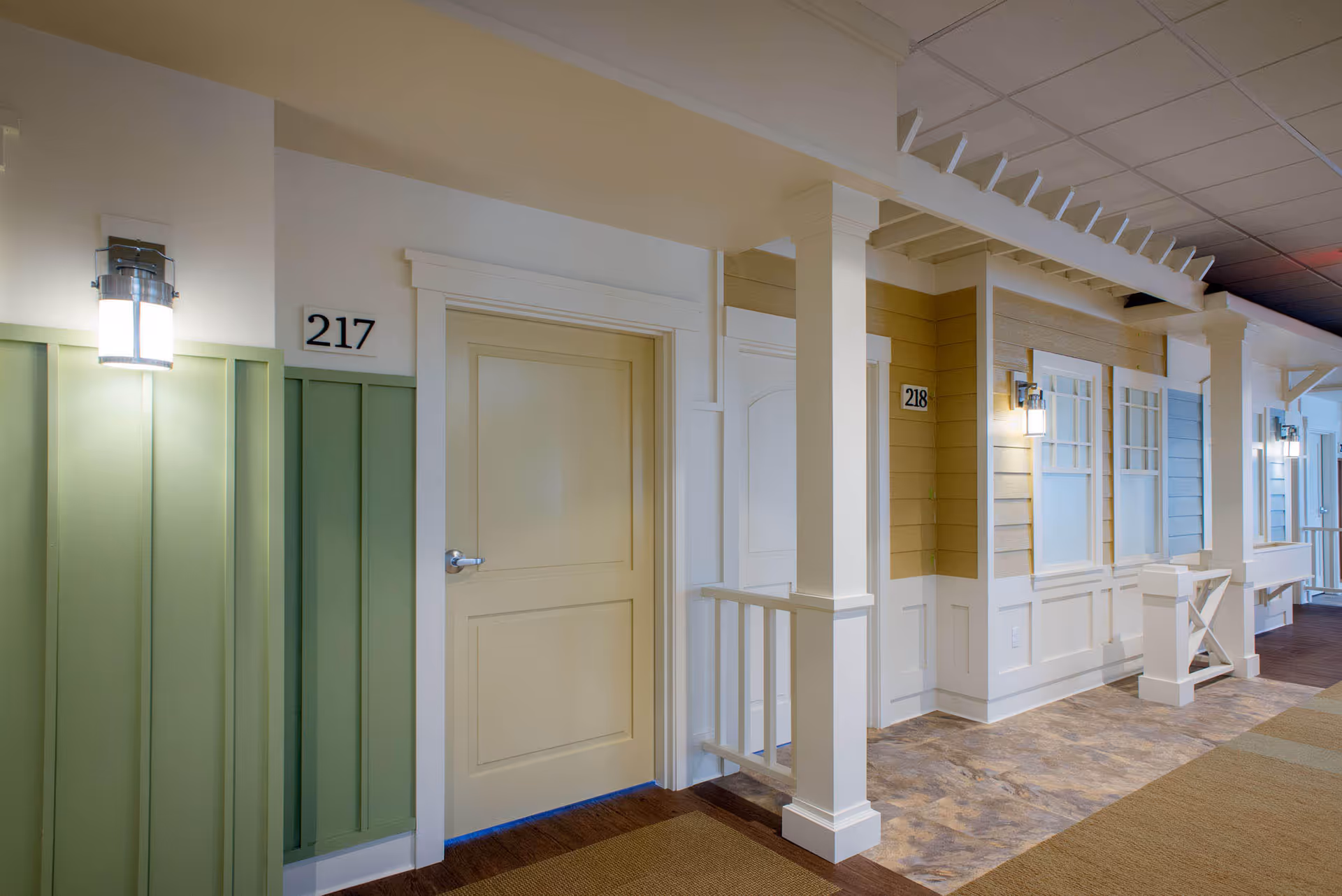 Bright interior corridor with pastel doors, columns, and warm lighting in a memory care facility.