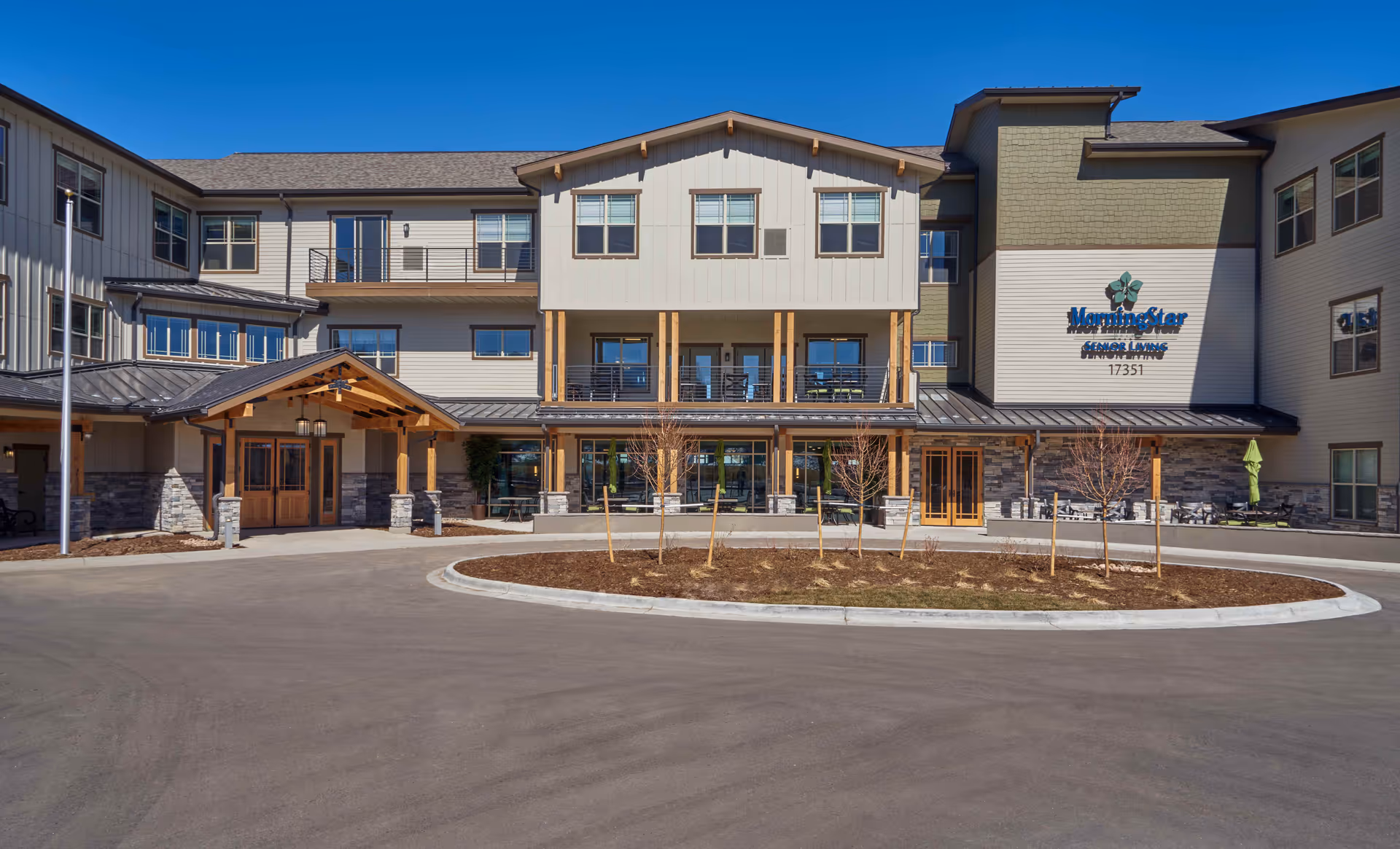 Front exterior view of MorningStar Senior Living of Arvada building with a circular driveway and small landscaped area with young trees in front.