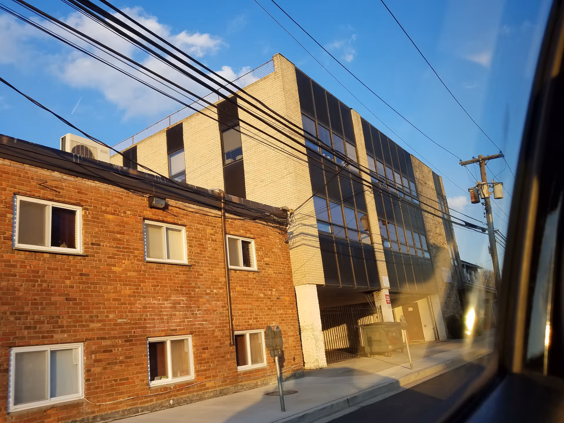 Two adjacent buildings, one brick and one glass-front, line a sunny urban street.