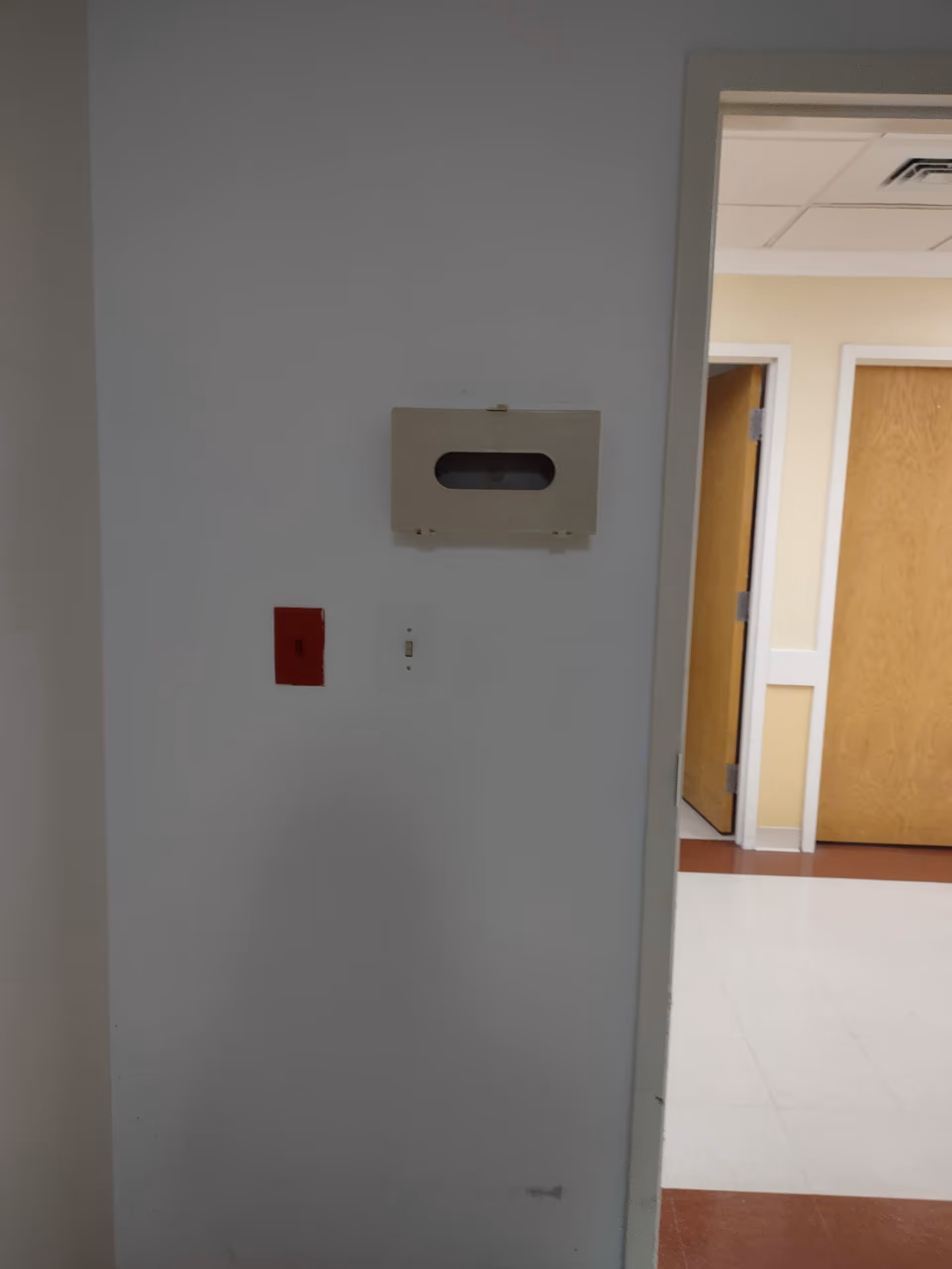 Interior corridor with doors, white walls, and a wall-mounted fixture.