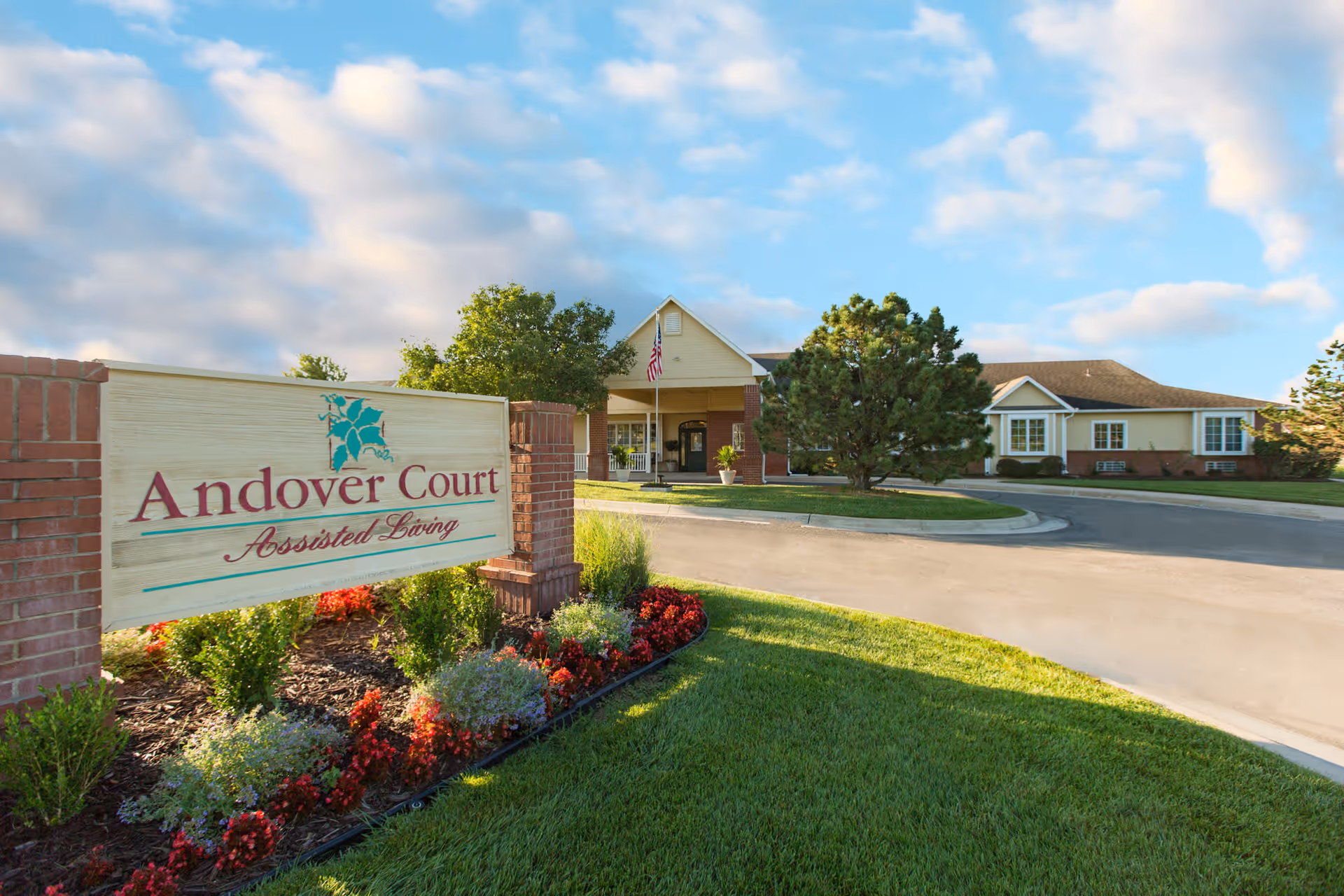 Front exterior of Andover Court assisted living with a sign, landscaped flowerbeds, and a driveway leading to the entrance.