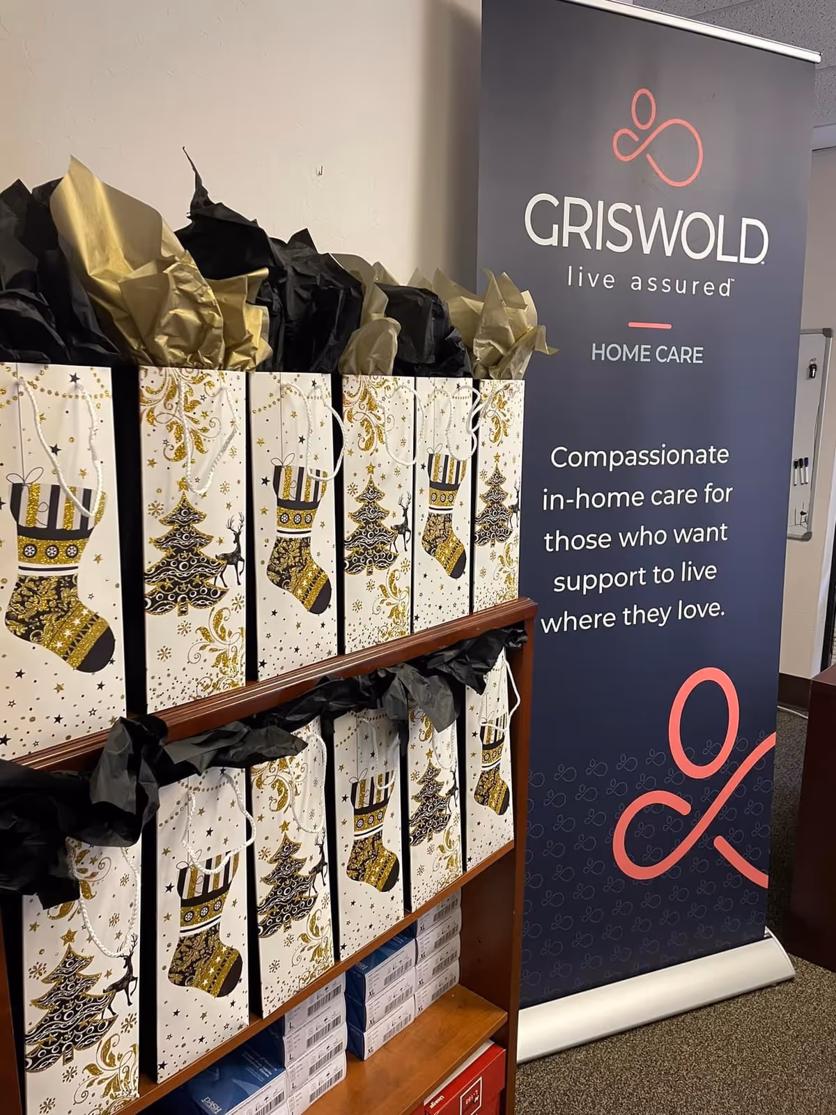 Row of decorative gift bags on shelves beside a Griswold Home Care banner