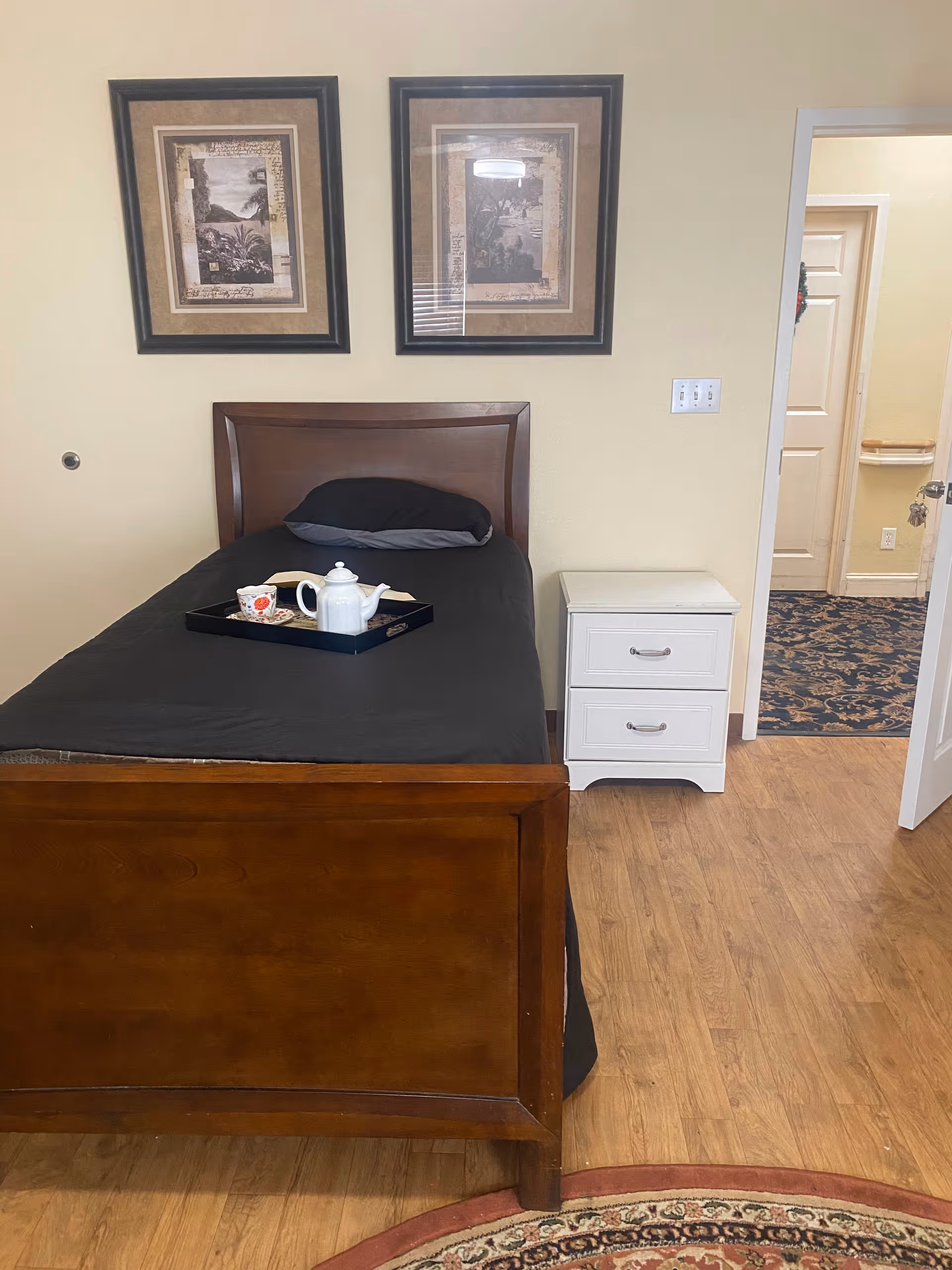A neatly made single bed with a black tray holding a teapot and cups.