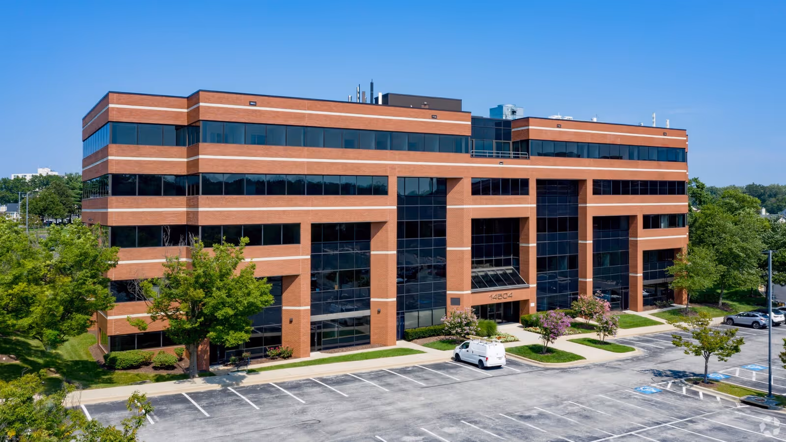 A brick, modern office building with glass windows and surrounding greenery.