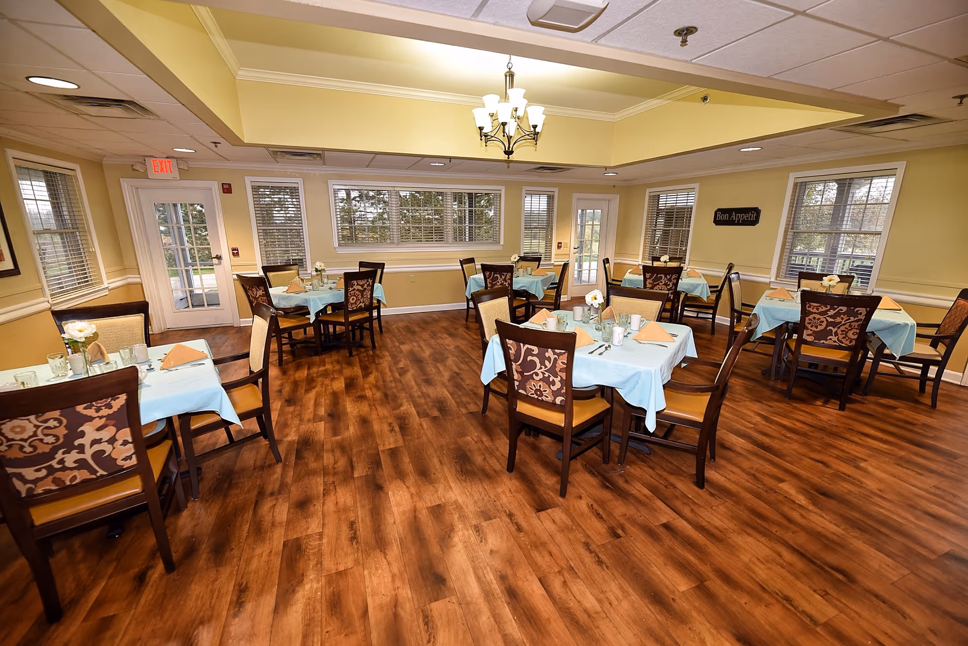 Bright dining room with several tables set for meals in a senior facility.