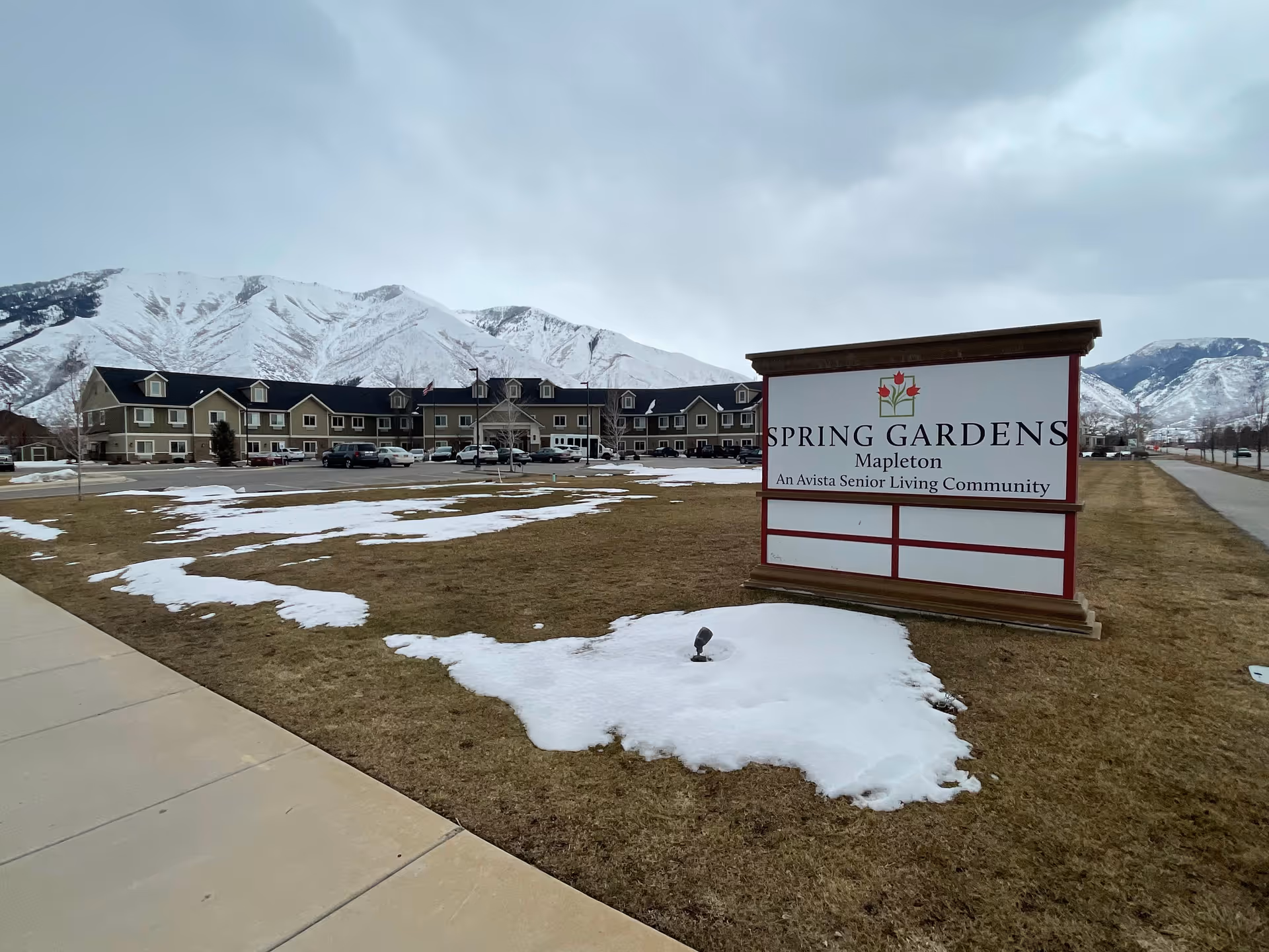 Snow patches dot brown grass around a large Spring Gardens Mapleton sign in front of facility.