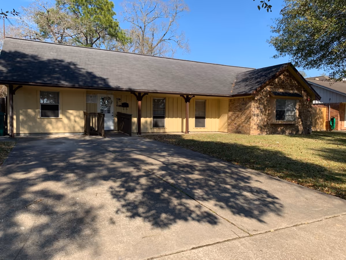 Single-story beige building with a covered porch and concrete driveway.