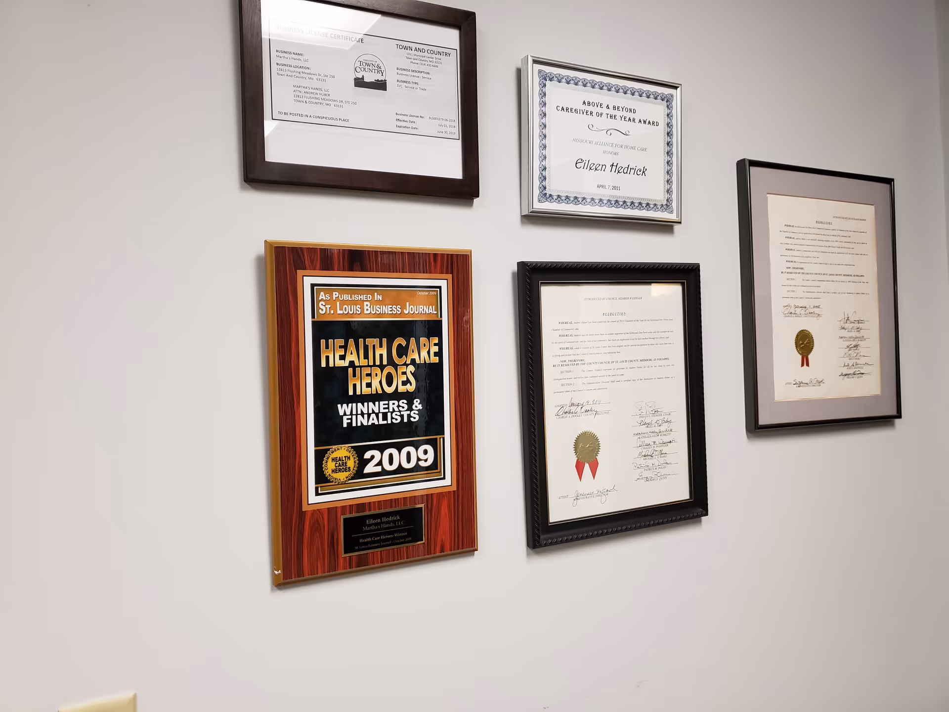 Wall with six framed certificates and awards hanging in a neutral room.