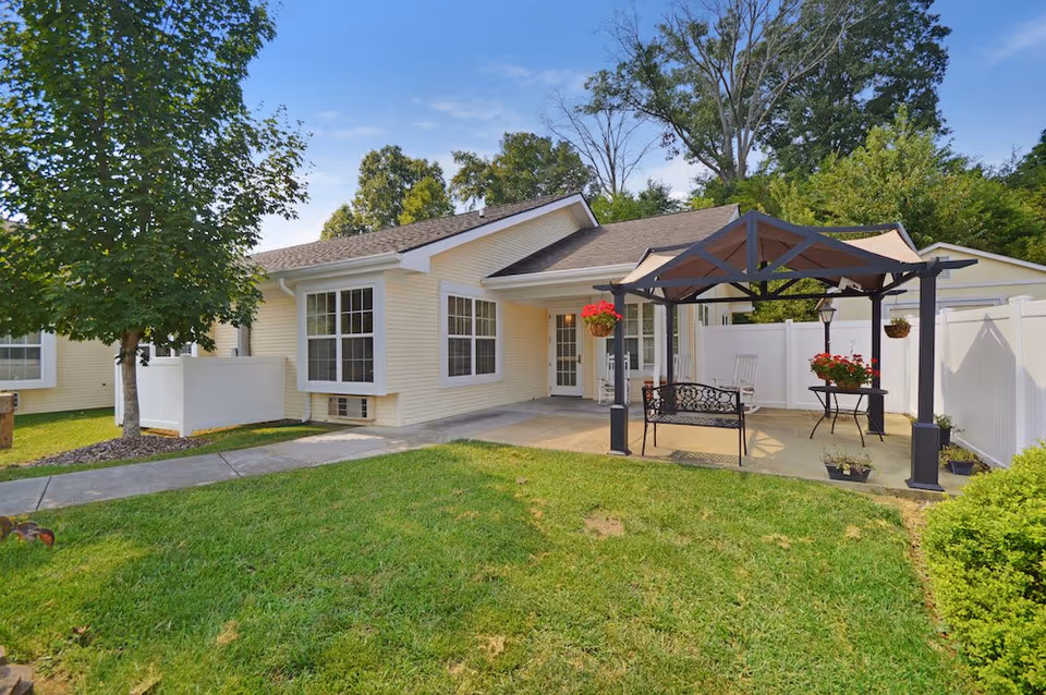 Single-story yellow senior living facility with a covered outdoor seating area and green lawn.