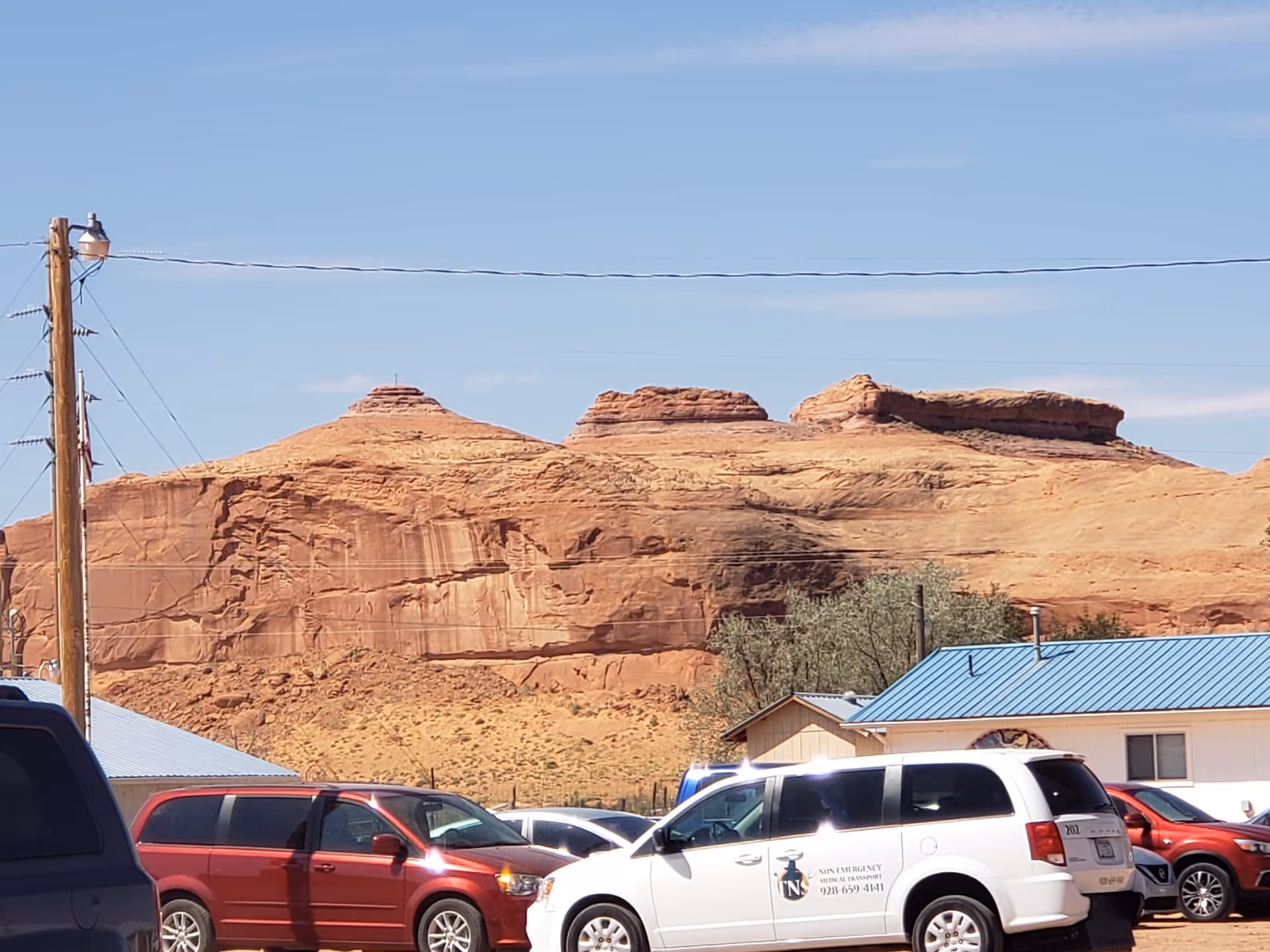 Parking lot with red rock formations and a blue-roofed building.