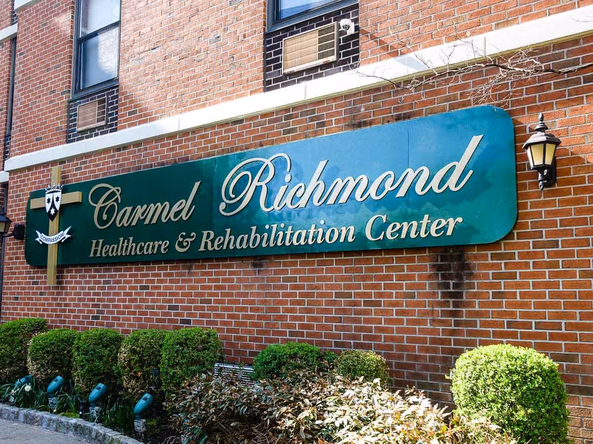 Brick building exterior with a large Carmel Richmond Healthcare & Rehabilitation Center sign and shrubs.