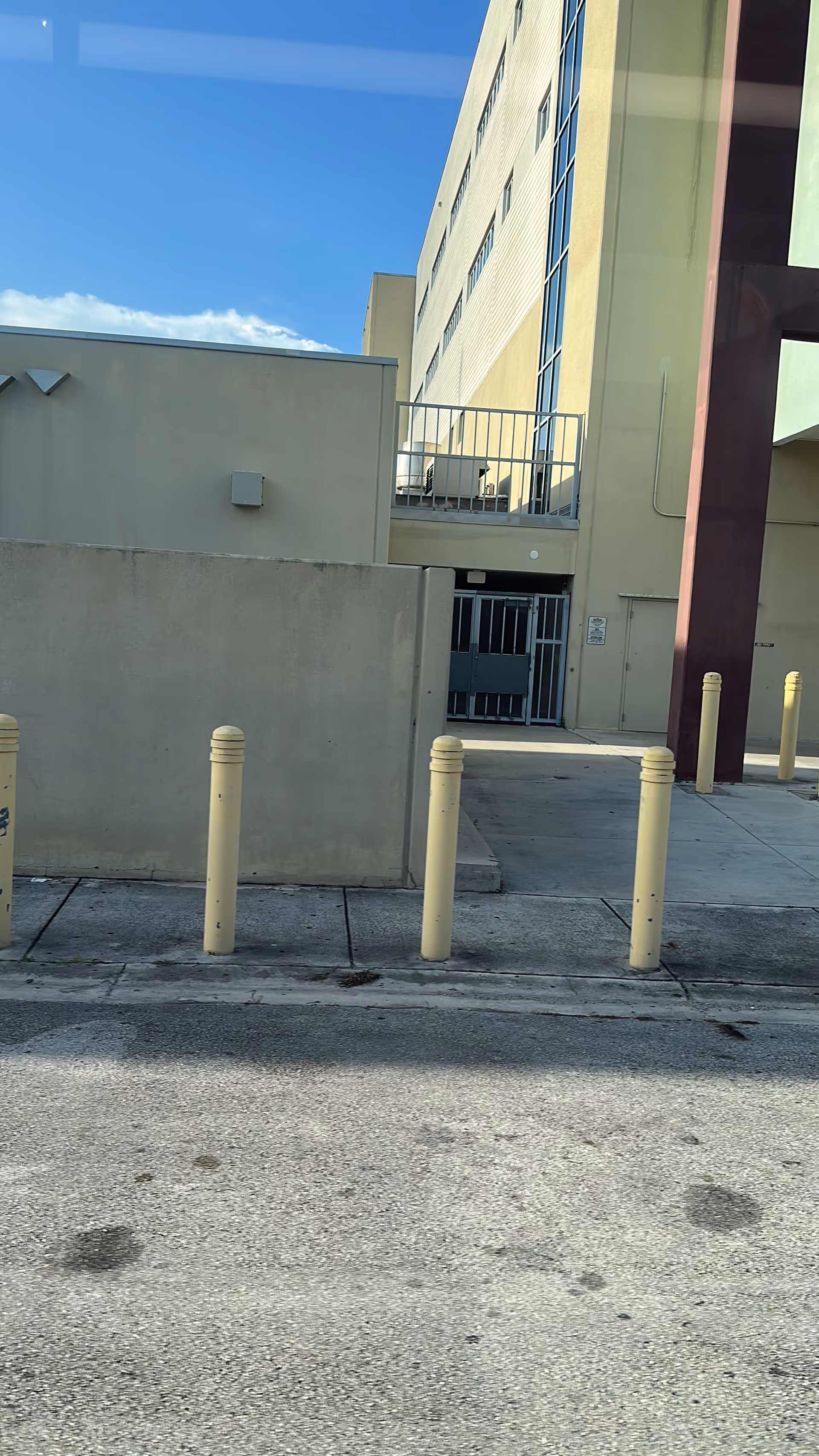 Exterior view of a beige senior facility facade with gate, bollards, and blue sky.