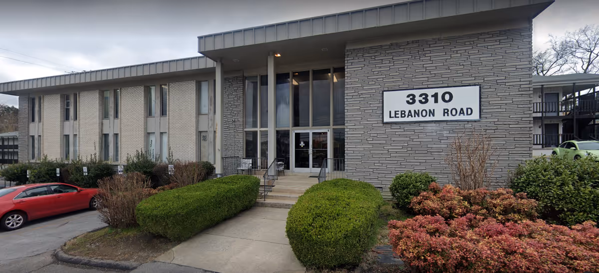 Exterior view of a senior living facility entrance with shrubs and signage.