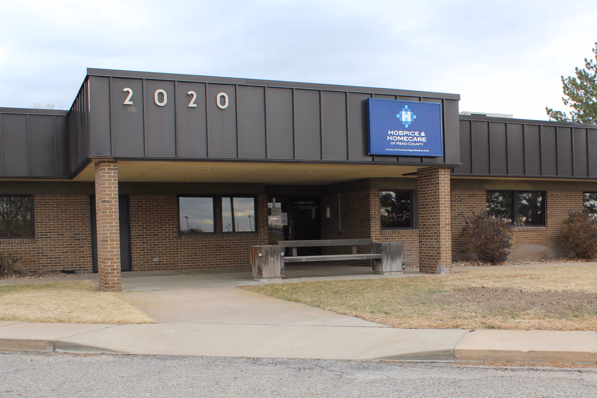Brick building with a covered entrance and a blue Hospice HomeCare of Reno County sign.