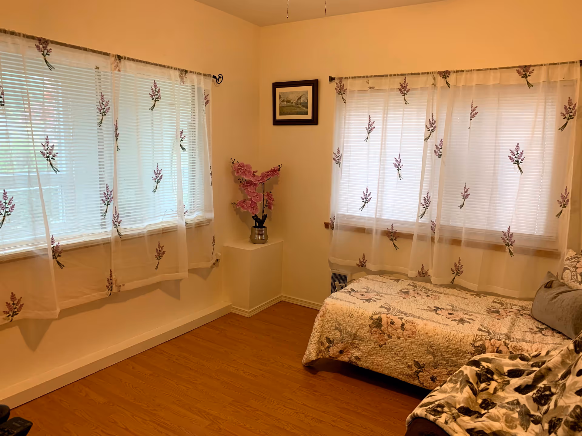 A cozy bedroom with two windows, a bed, and floral decor.