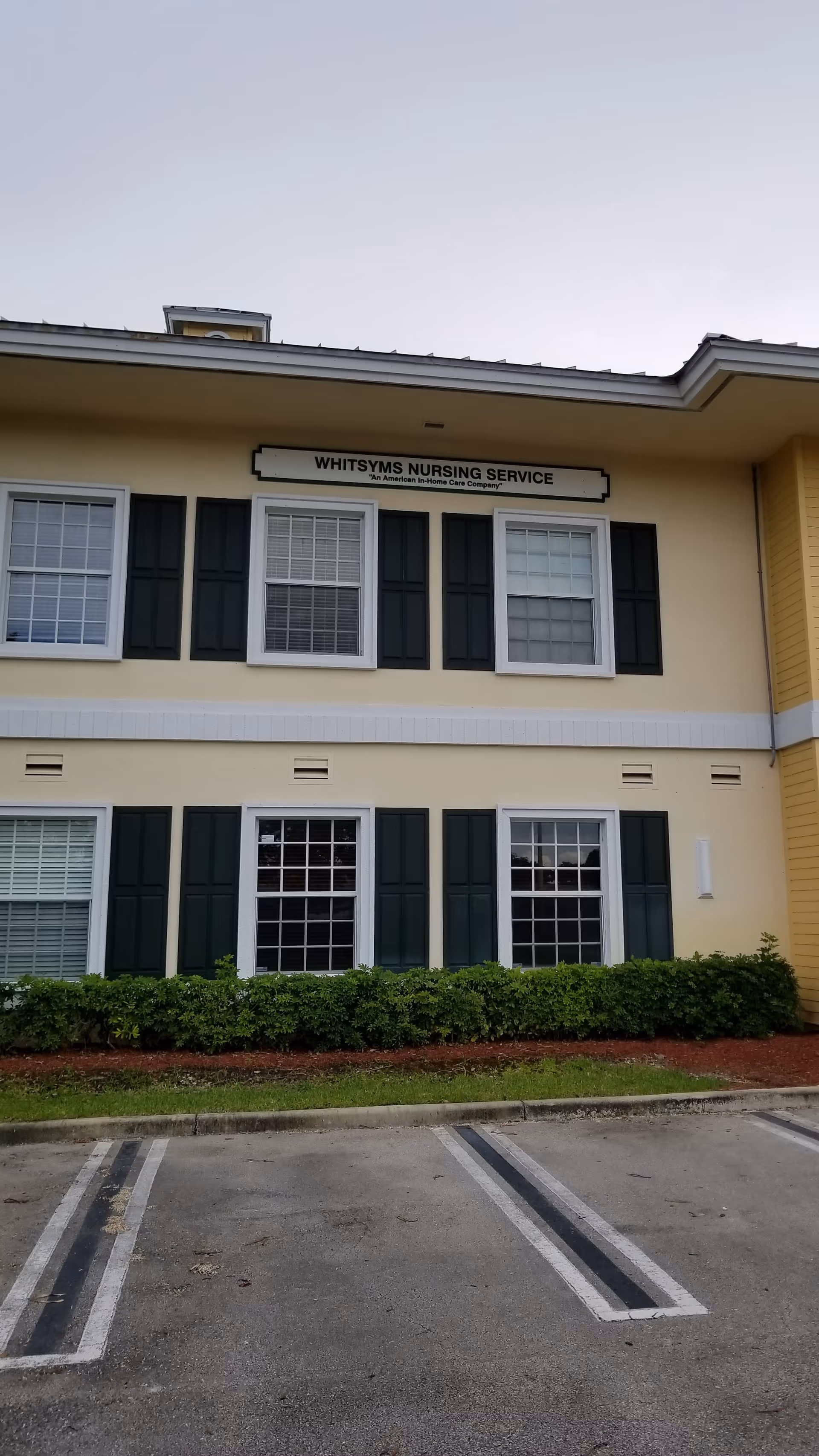Two-story beige building with green shutters, Whitsyms Nursing Service sign, parking lot in front.