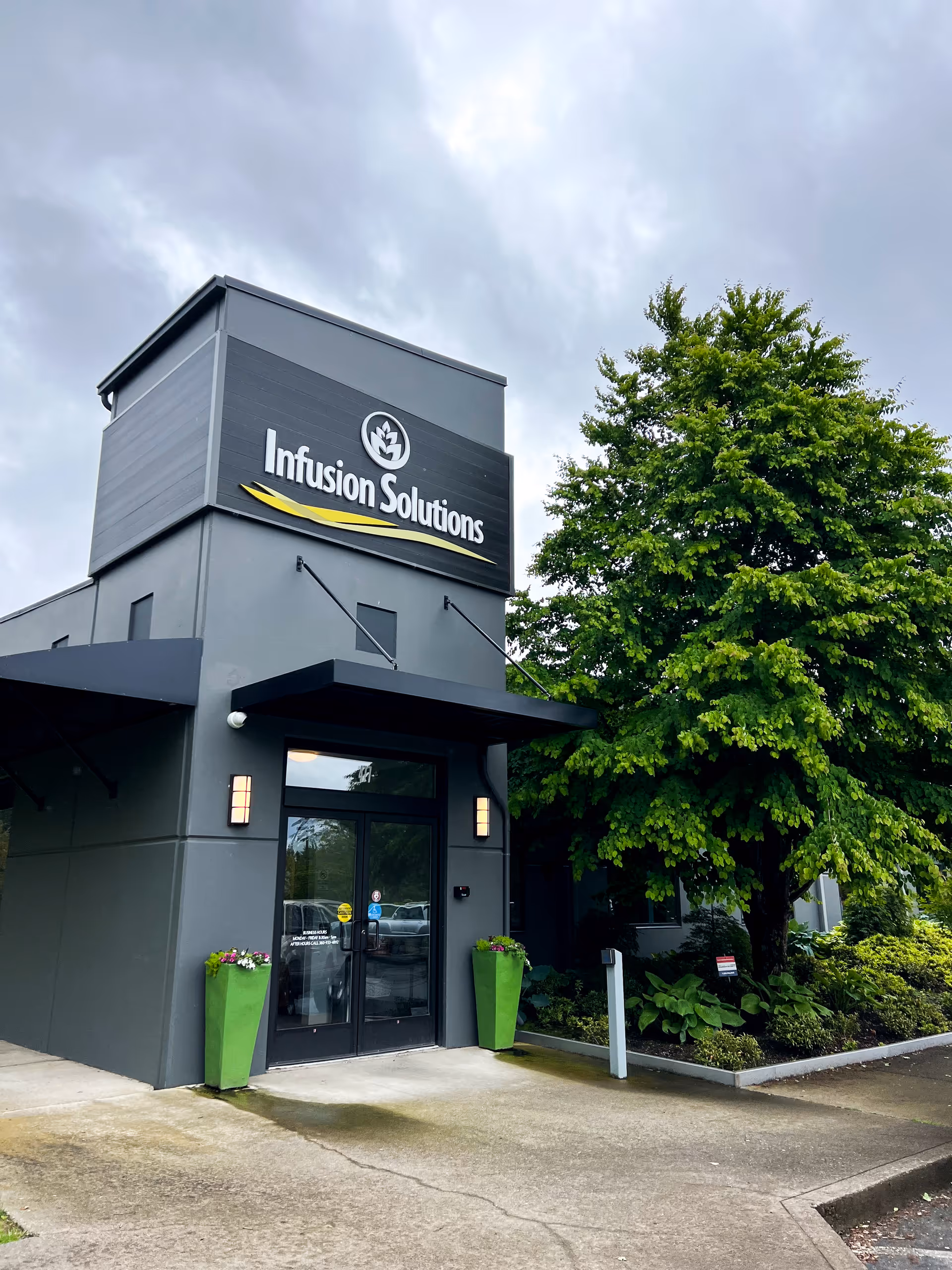 Modern medical facility entrance with Infusion Solutions sign and green planters.