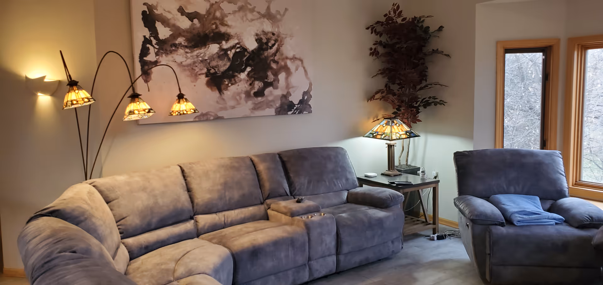 Cozy living room with a blue sectional, lamps, wall art, and large windows.