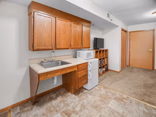 Compact kitchen area with wooden cabinets, sink, microwave, and stacked appliances beside a doorway.