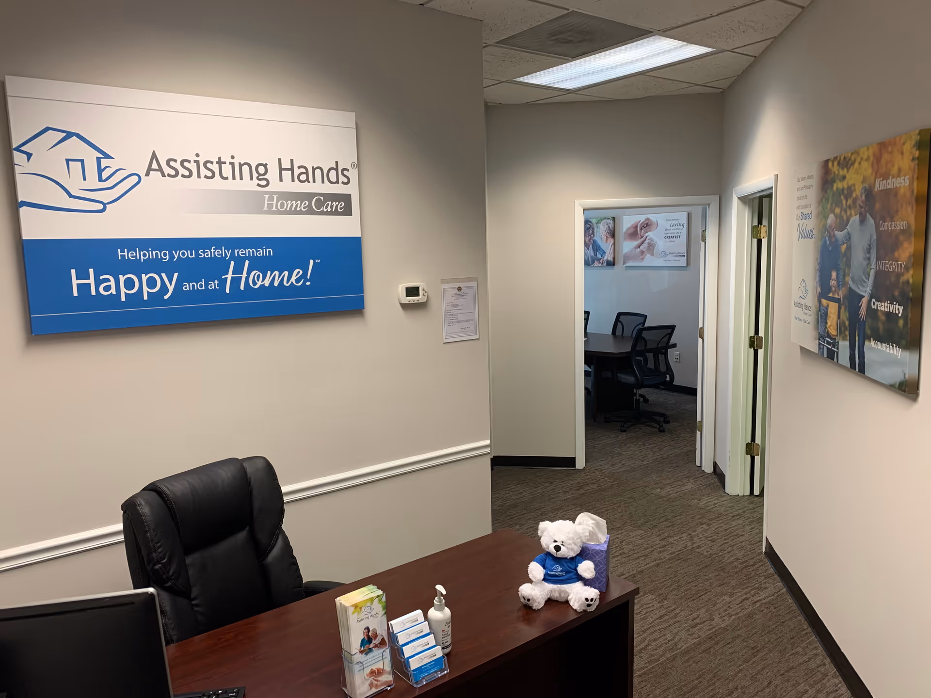 Reception area of Assisting Hands Home Care Baltimore with desk, sign, teddy bear, and hallway.