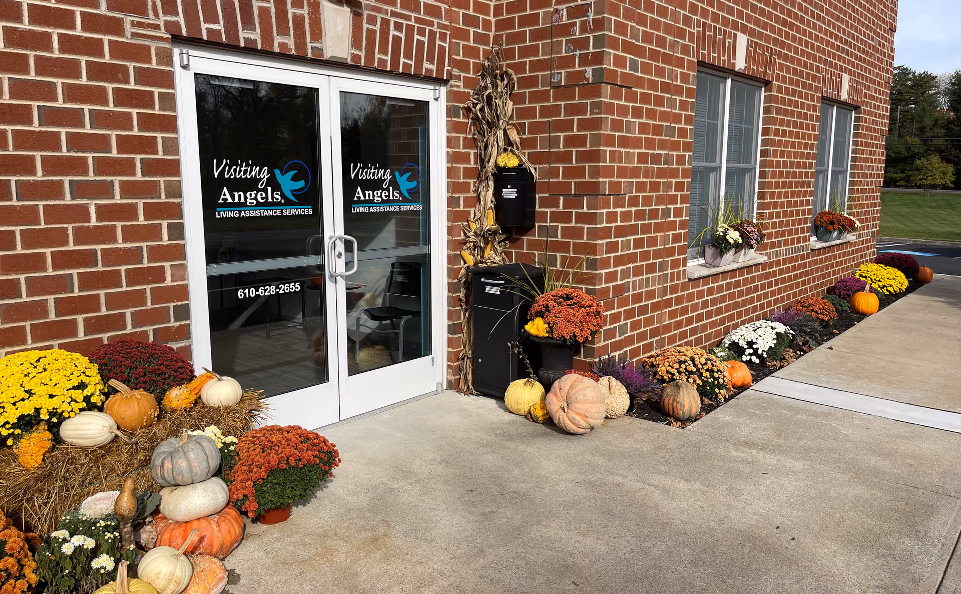 Brick building entrance of Visiting Angels with pumpkins and fall flowers along the walkway.