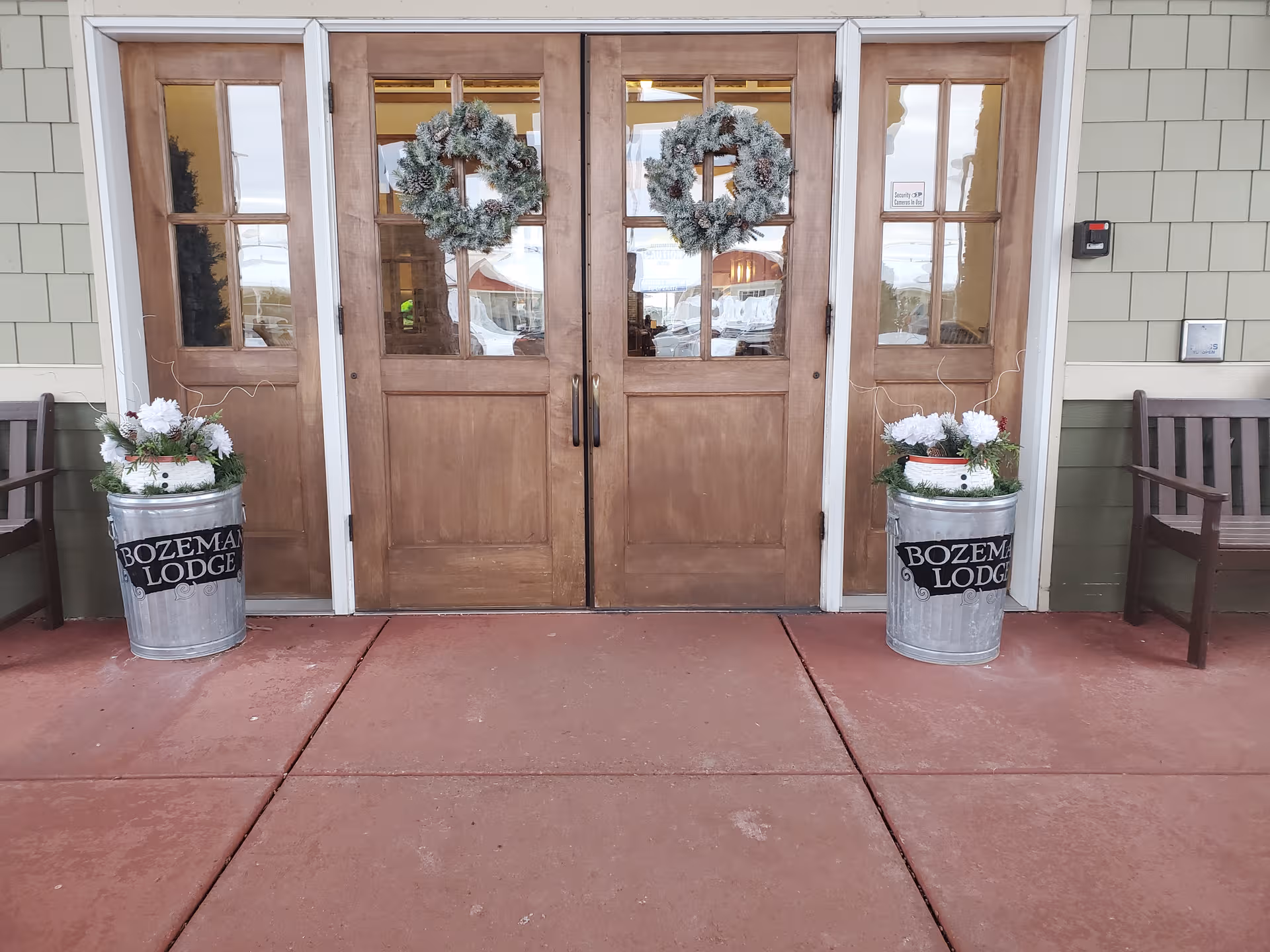 Wooden double doors with wreaths and metal planters labeled Bozeman Lodge at front entrance.