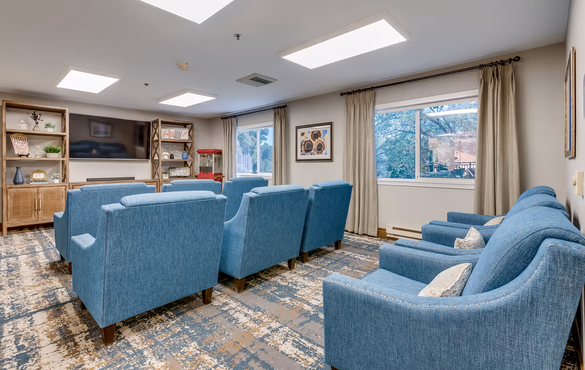 Blue upholstered chairs and sofas arranged in a spacious senior living common room with a window.