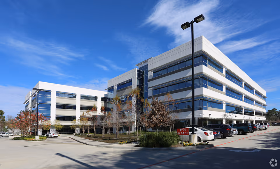 Modern, glass-fronted senior living facility with parking lot under a blue sky.