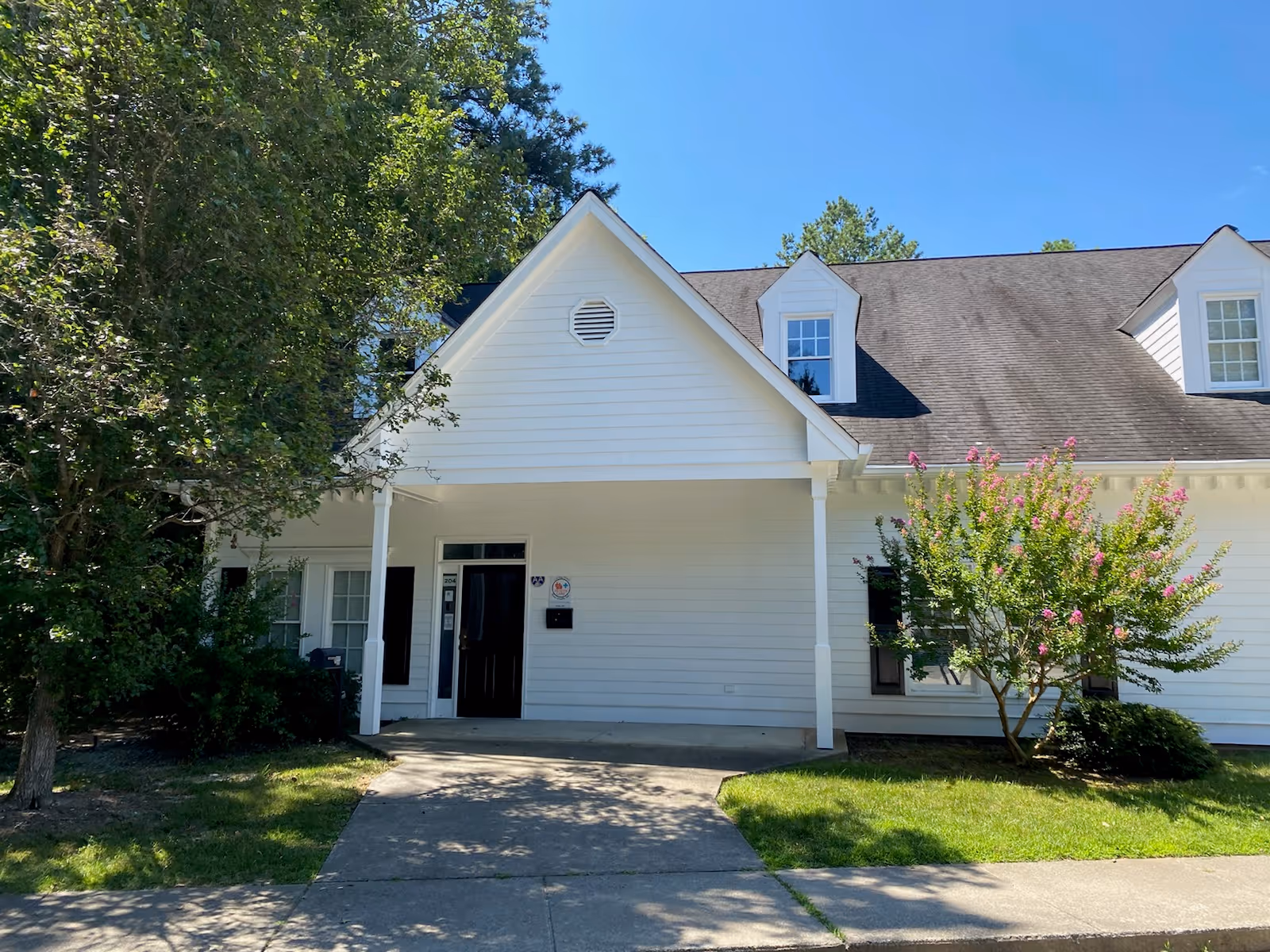 White residential-style facility with a front entrance, porch, and surrounding trees.