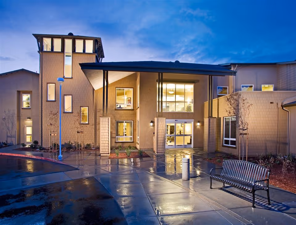 Exterior view of The Parkview senior living entrance at dusk with a bench nearby.