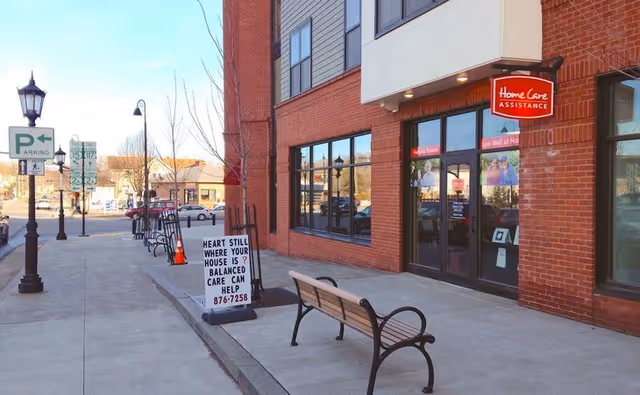 Exterior view of Home Care Assistance storefront on a brick building with benches along the sidewalk.