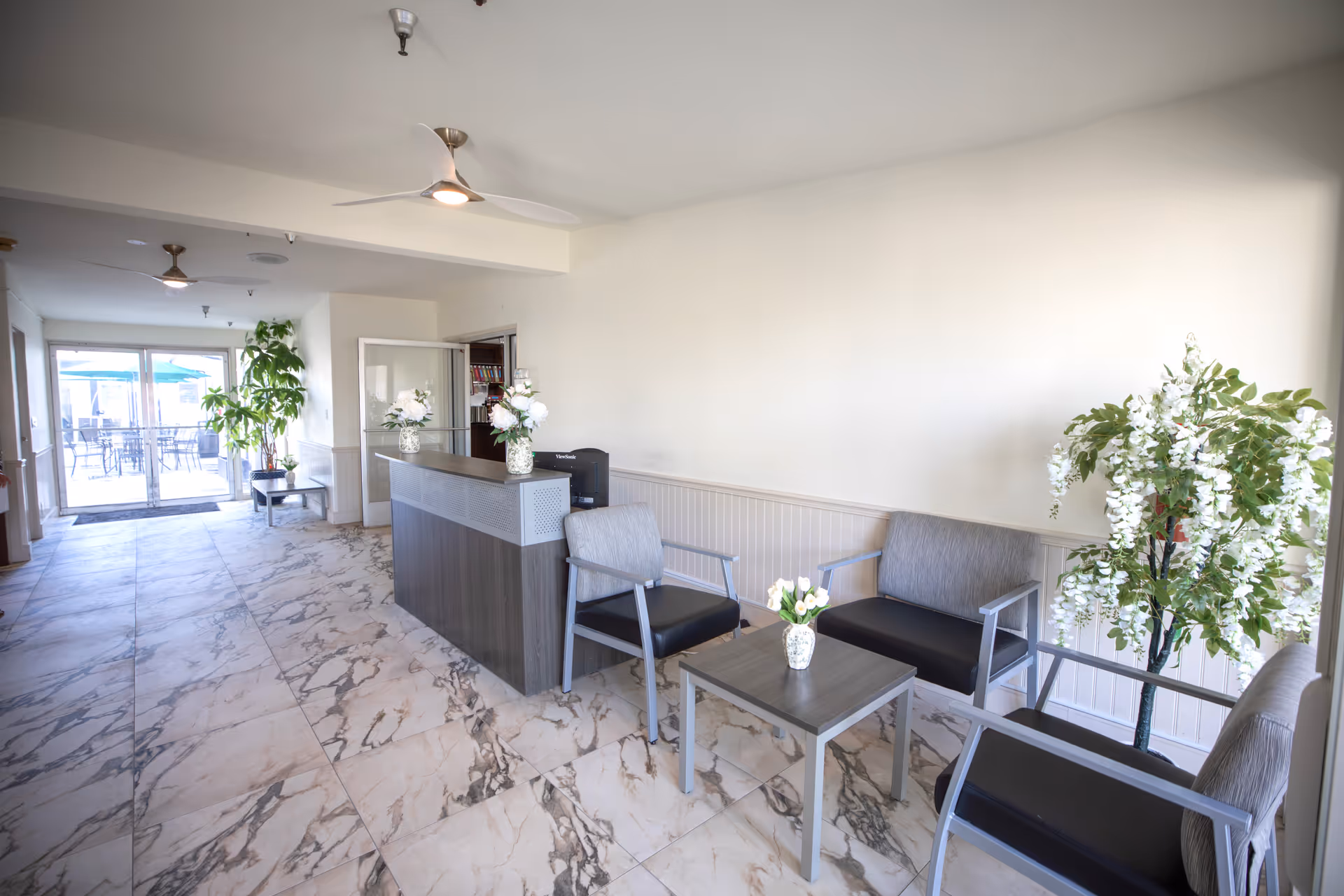 Bright reception lobby with marble floors, seating area, potted plants, and glass doors to patio.