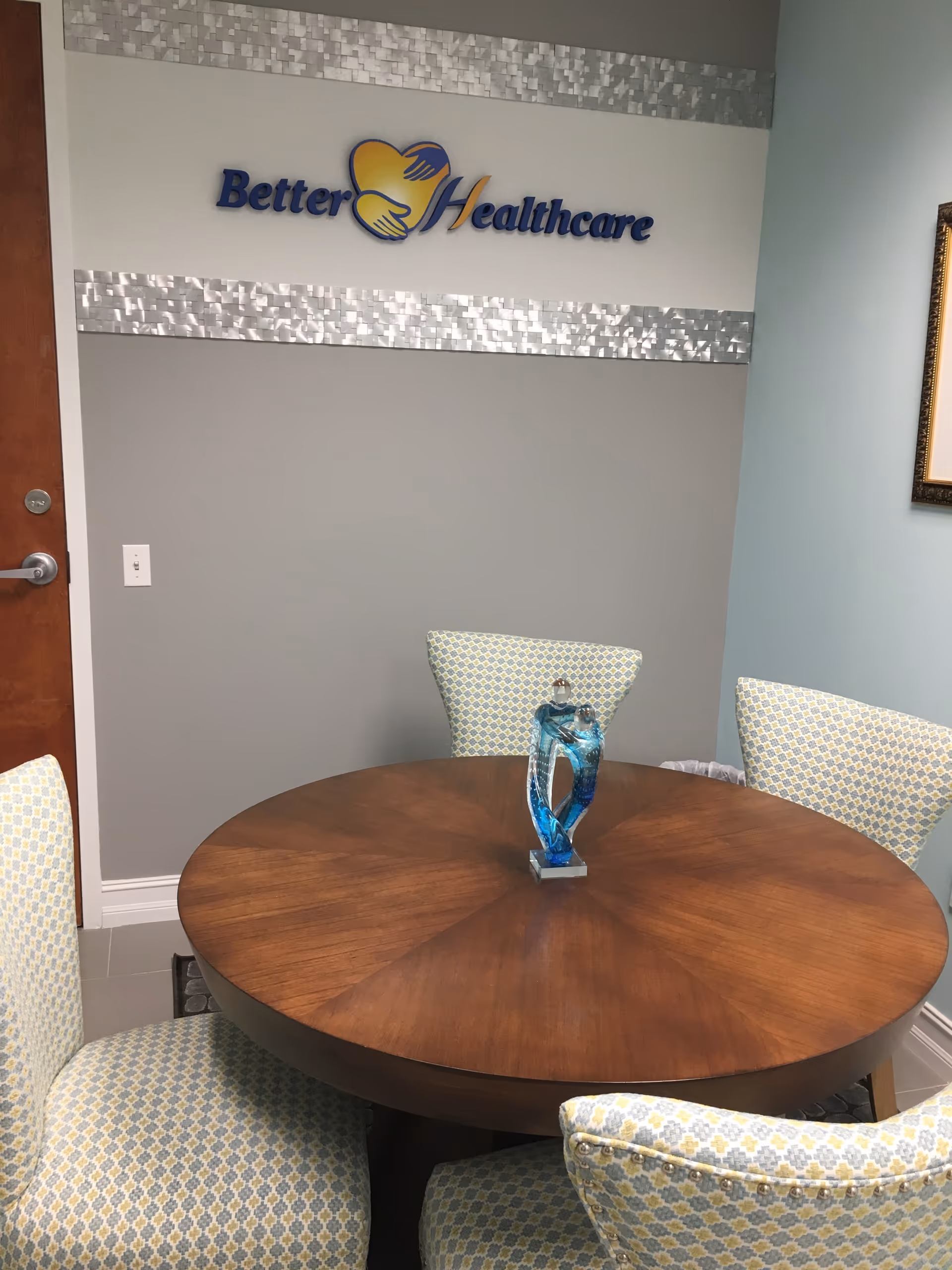 Round wooden dining table with four patterned chairs in a lounge area at Better HealthCare.